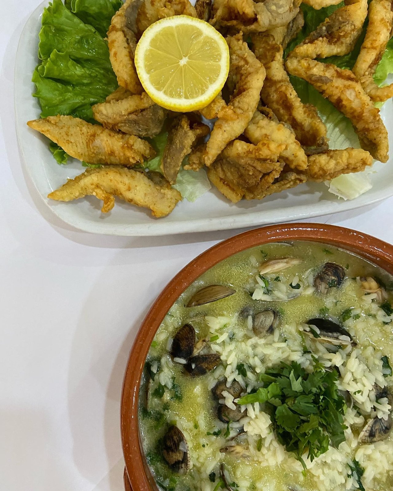 Filetes de peixe-galo fritos com limão e alface, e um tacho de barro com arroz de amêijoas