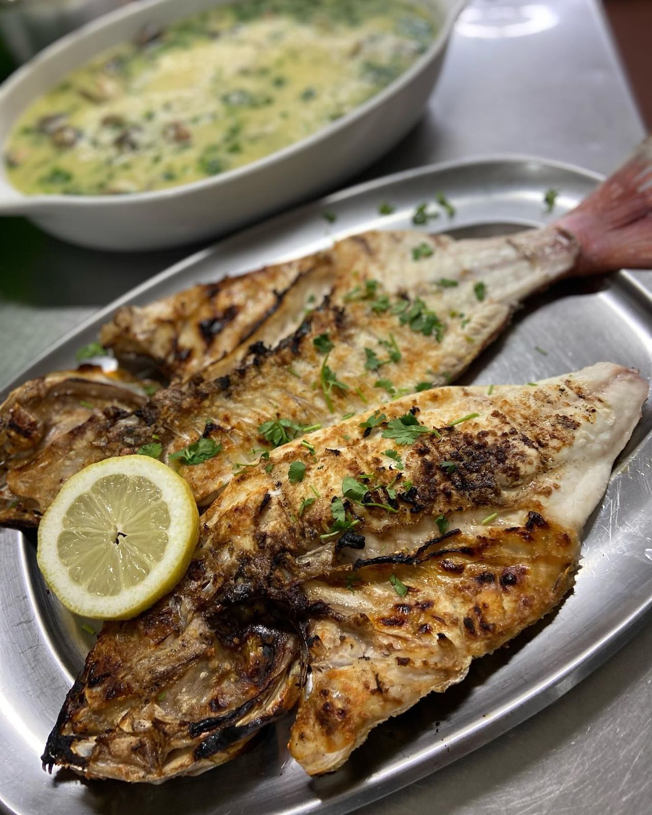 Pargo grelhado aberto numa travessa, com limão e salsa, e arroz de amêijoa ao fundo